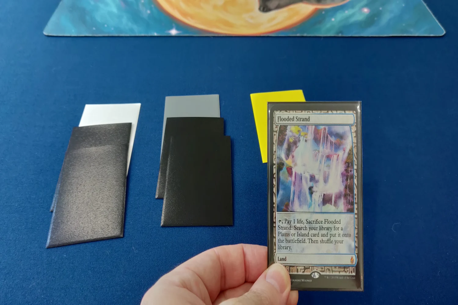 Winston draft with two stacks of face-down cards while a hand is holding a Flooded Strand